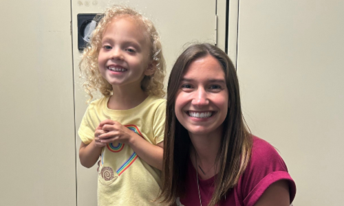 Avery and Speech Therapist Cassie smiling in front of a tan background.