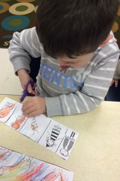 Kolton carefully using scissors to cut apart a worksheet that has been colored with crayons.