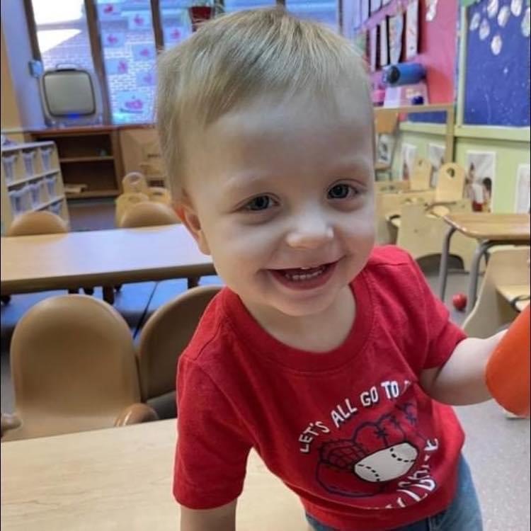 Colton smiling wearing a red shirt in a classroom.
