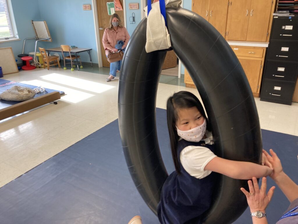 Ellery swinging in a circle shaped swing in physical therapy.