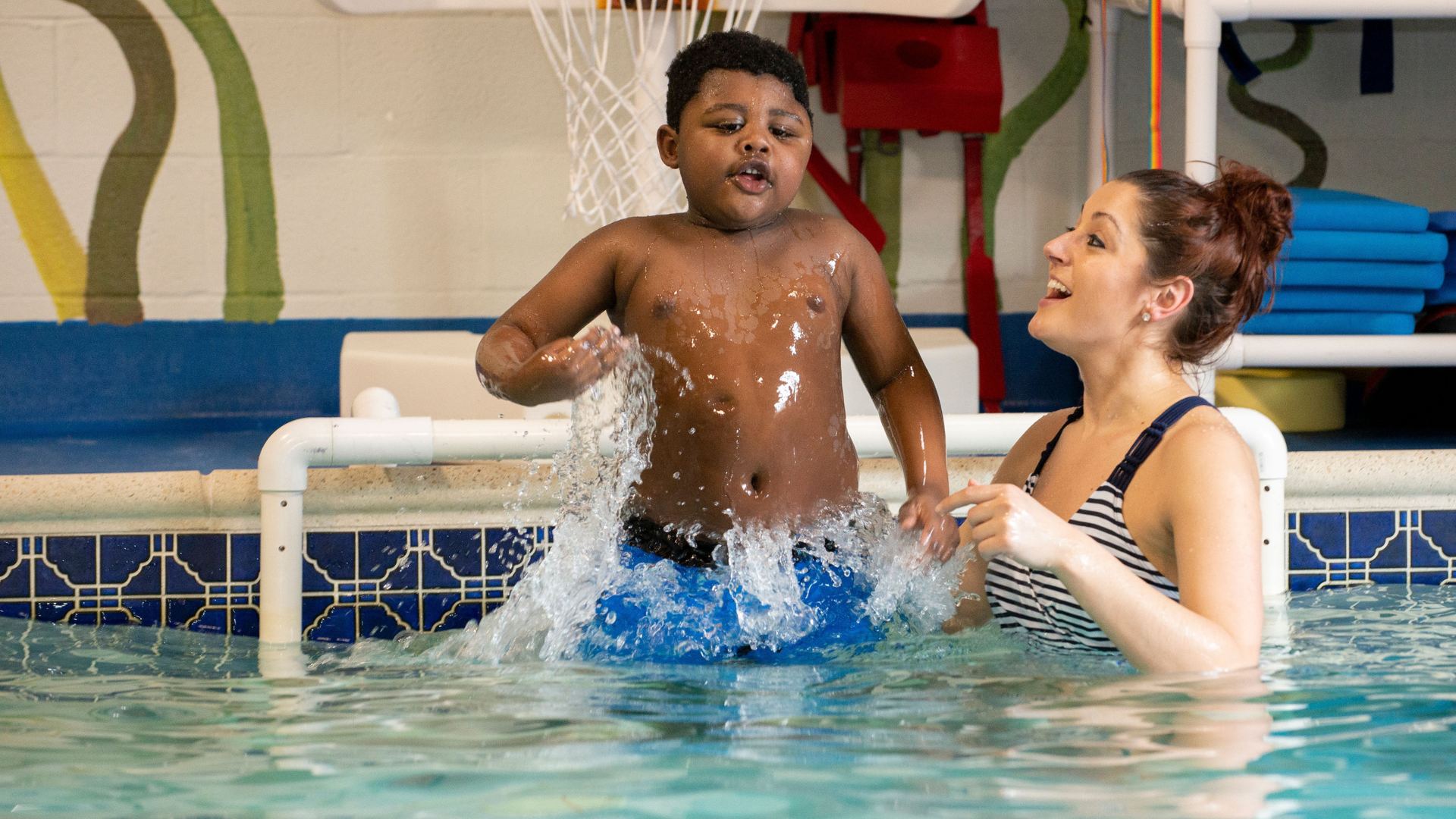 A child in a pool with a therapist working on an exercise.