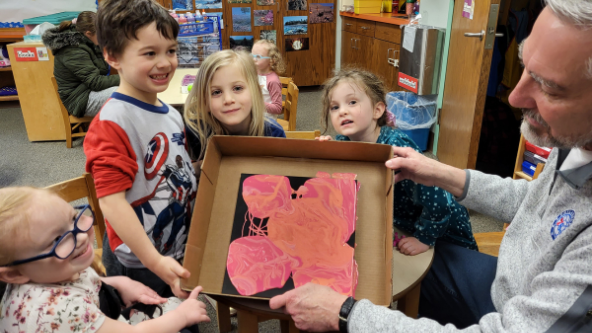 middle aged volunteer showing pre-schoolers a painting art project