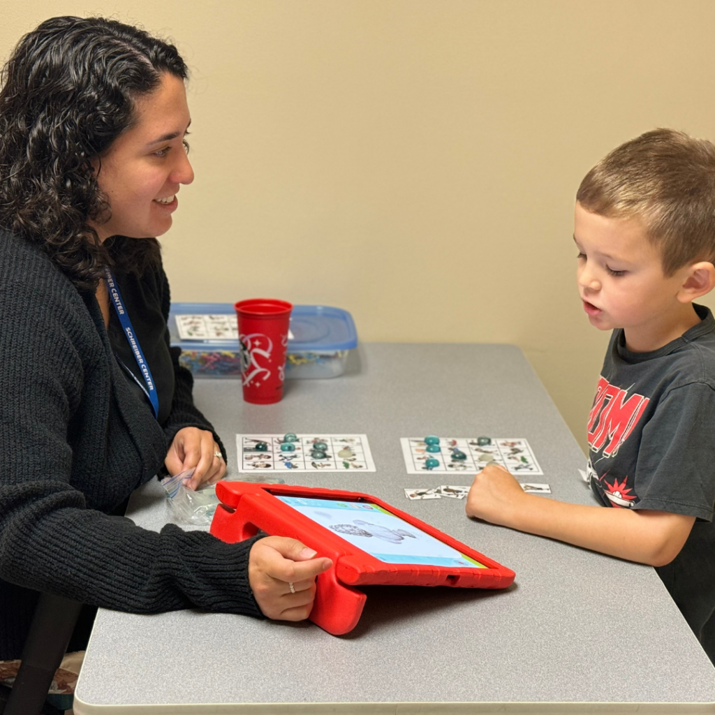 A therapist holding a tablet while a child reads and completes an exercise.